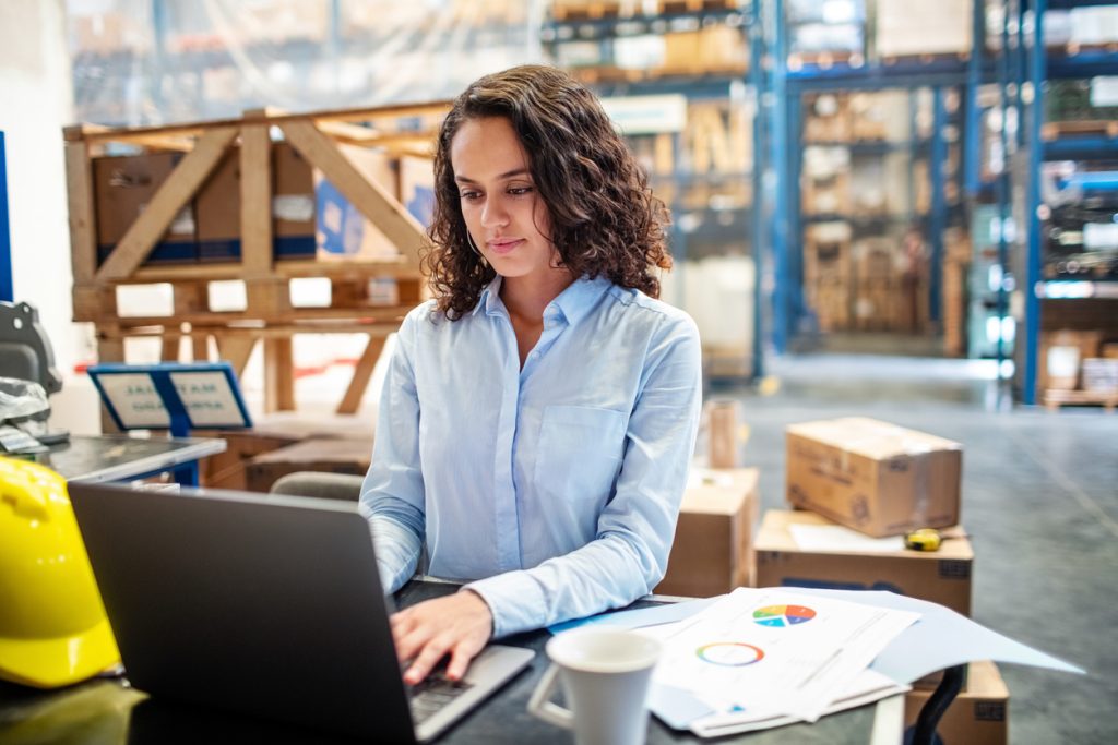 woman in warehouse using laptop for supply chain management